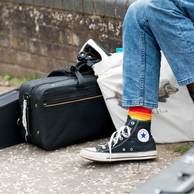 A pair of legs wearing stripy rainbow coloured socks and converse shoes